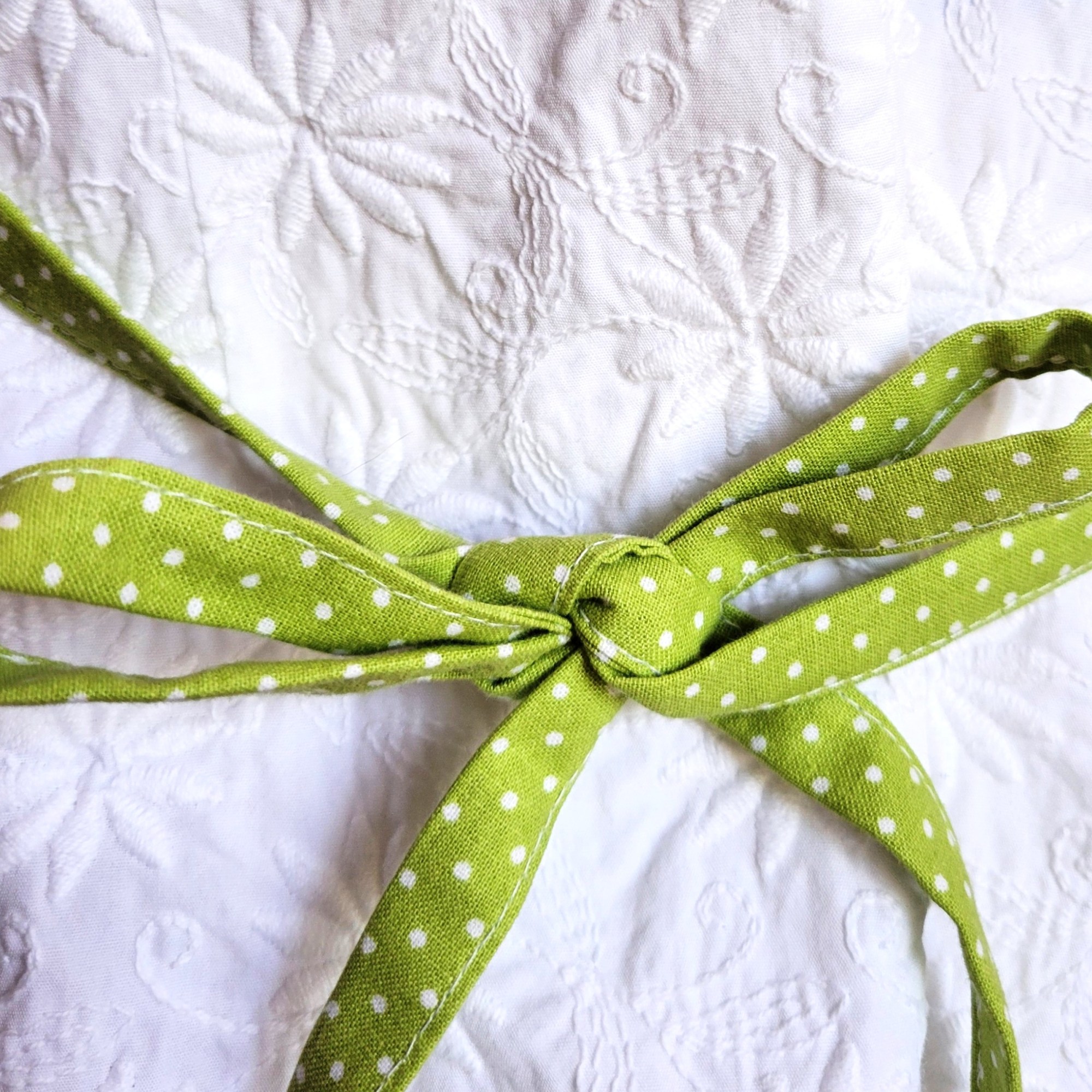 close-up photo of lime-green with small white poka dots fabric ties on apron and white embossed fabric background