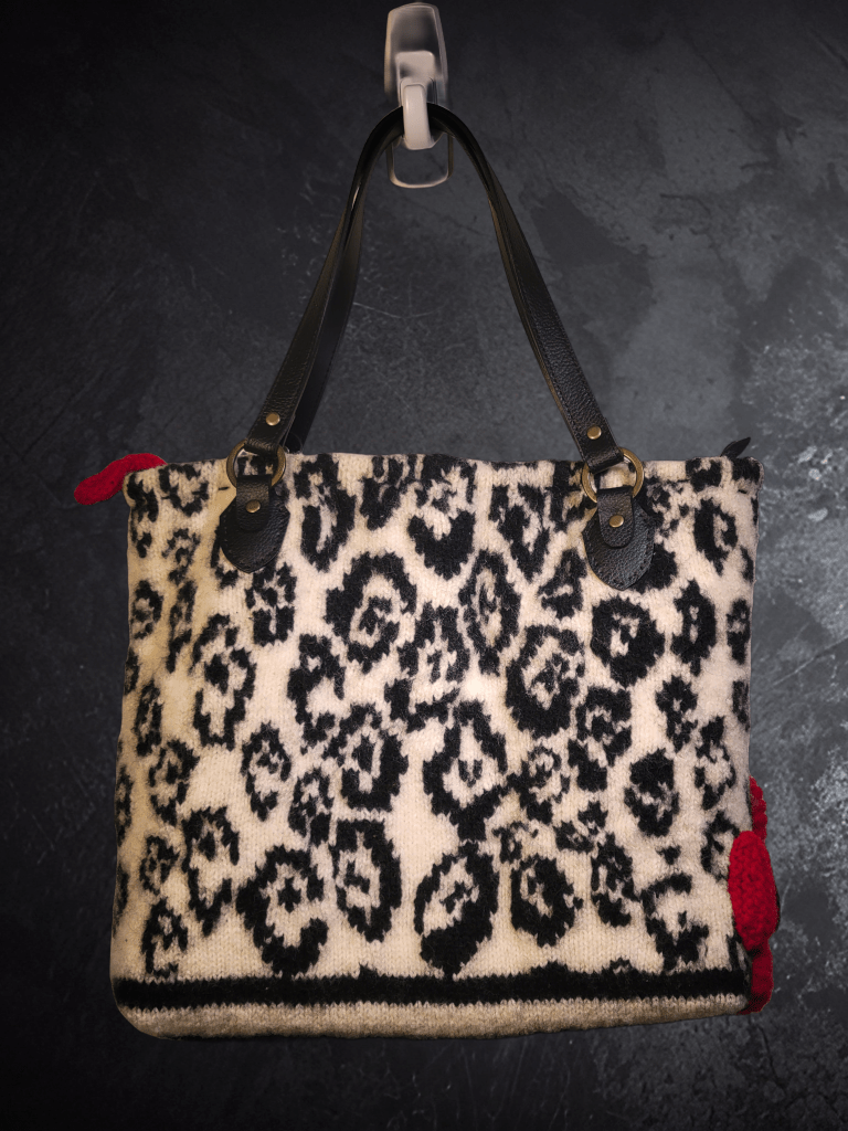 photo of upcycled tote bag or handbag from discarded textile wool sweater with red knitted flower on lower right with black faux leather straps